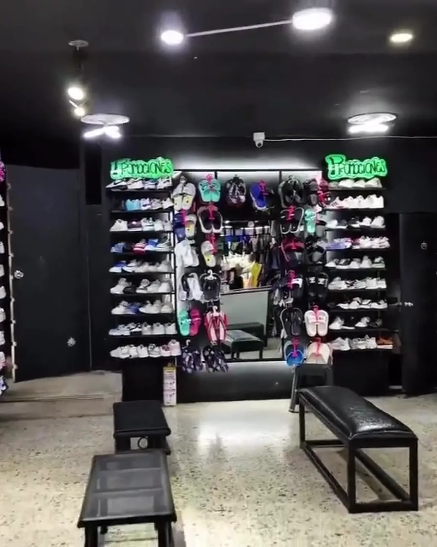 Interior de La Tienda de Óscar y Mateo en Ibagué: estanterías con tenis y sandalias de pared a pared, bancas para probarse el calzado y letreros de neón de promociones